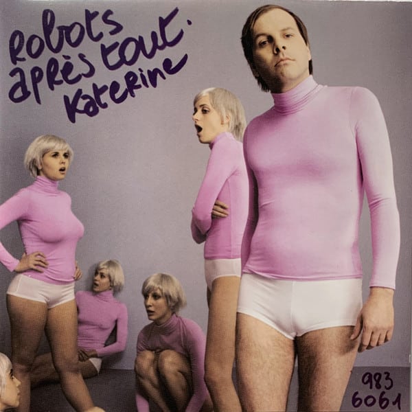 Part of Worst Record Covers. Several people with the same platinum blonde bob are all wearing pink roll-neck sweaters and short white shorts. One man closest to the front has dark hair instead, but is dressed the same.