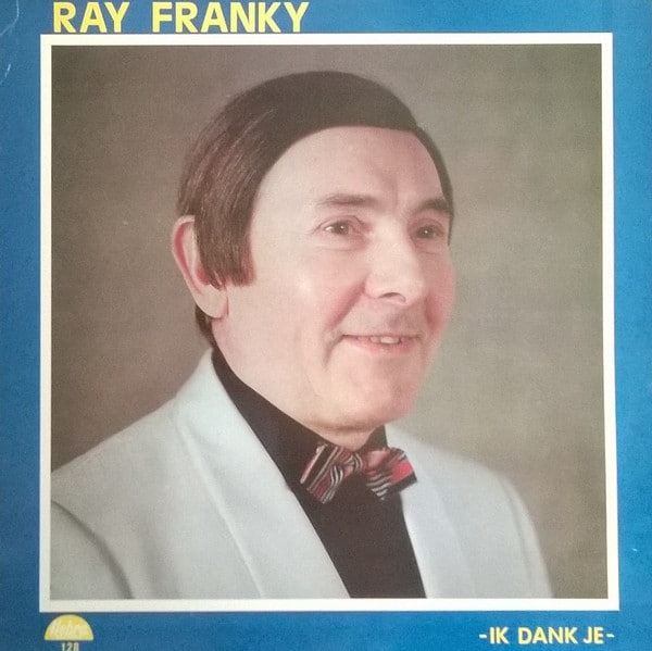 Part f Worst Record Covers. A man in a light grey suit jacket, black shirt and bow tie is posing and smiling. He has a very off combover.