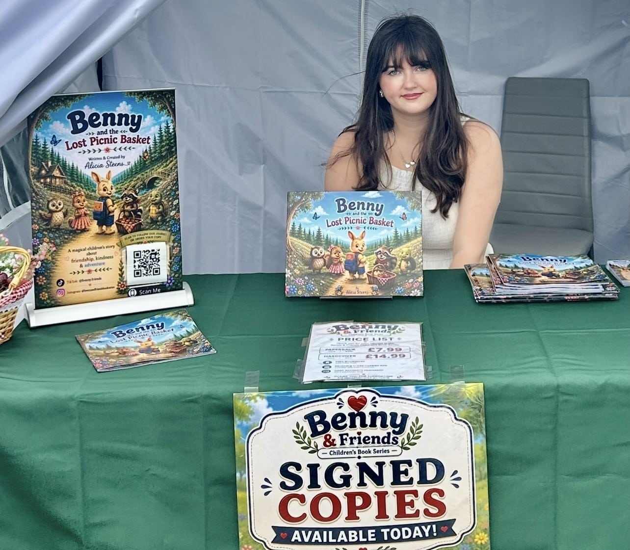 a lady with long brown hair sitting at a table with a green table cloth with books ton the top