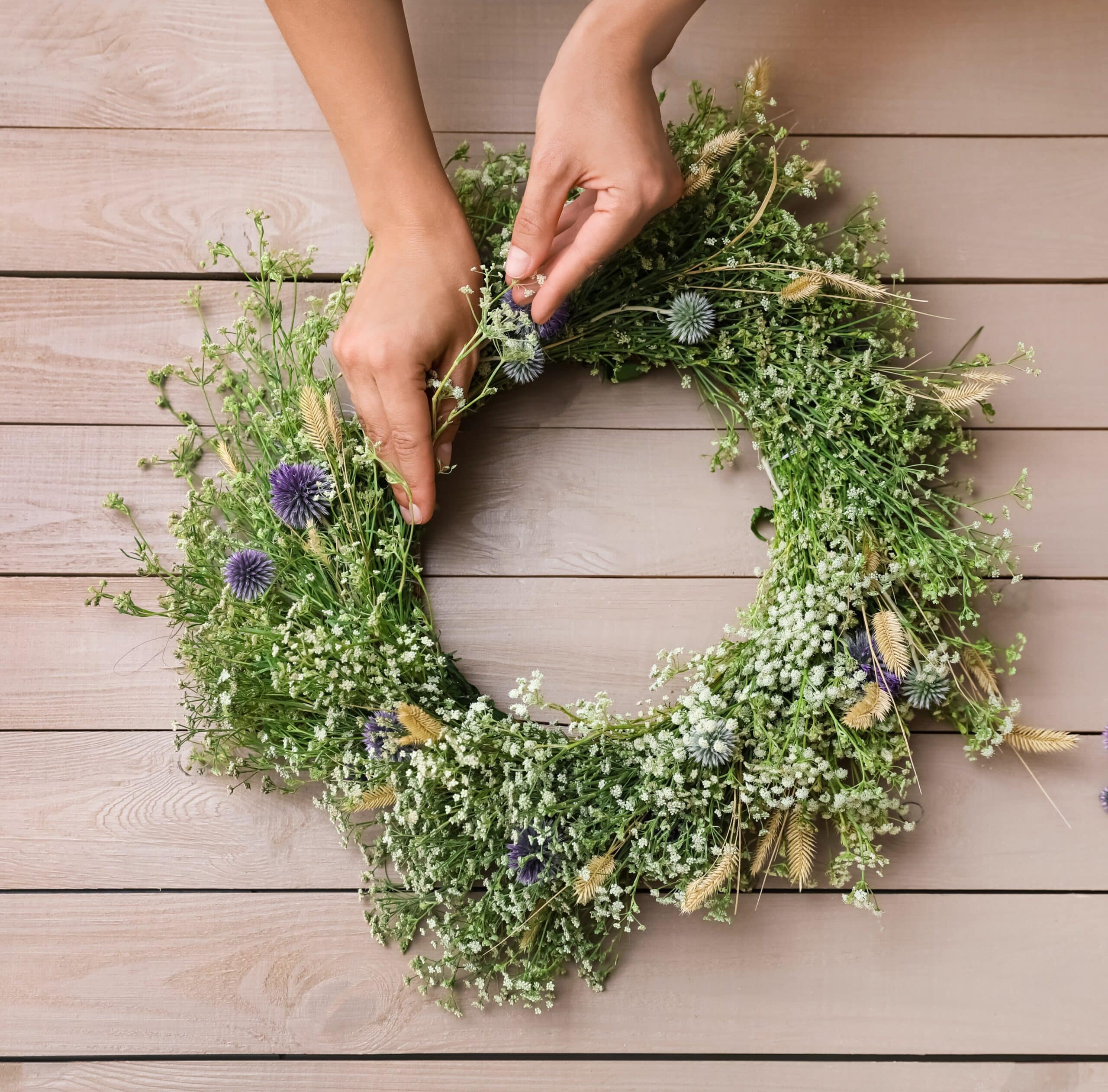 stock photo of a wreath of spring flowers being made on a wooden bench just the hands coming down from the top.