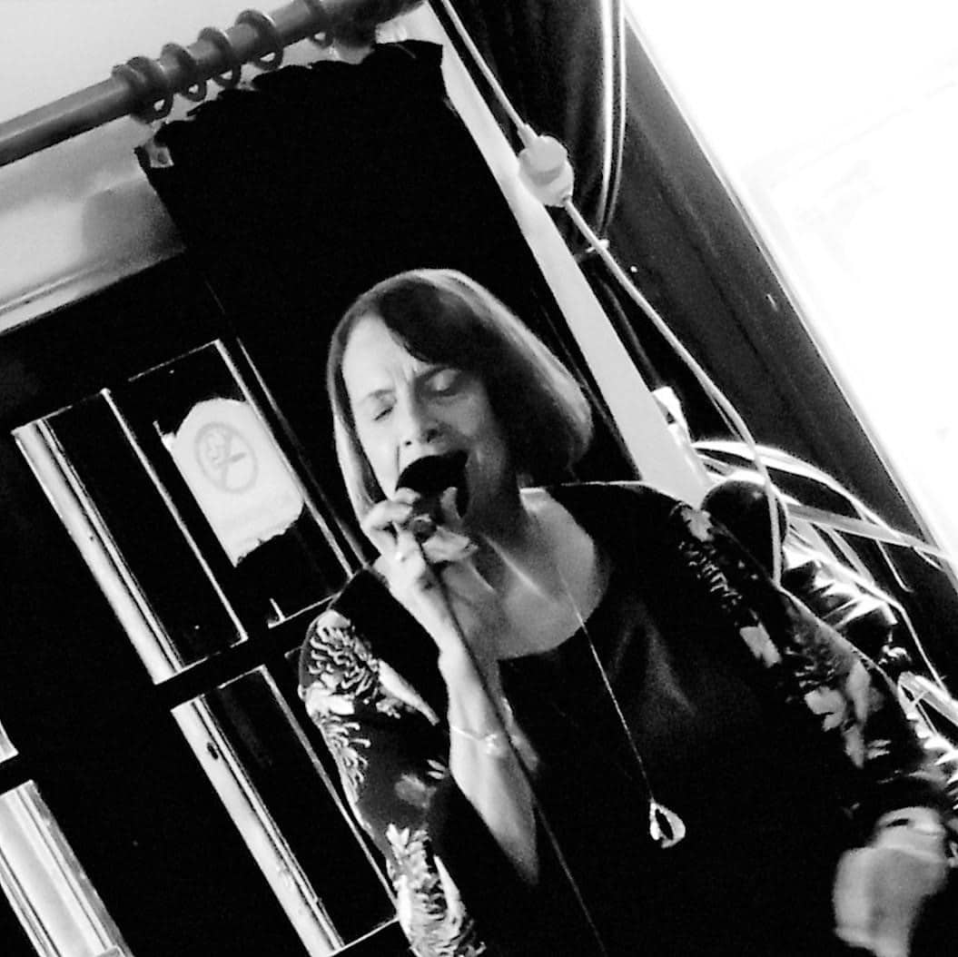 black and white photo of jazz singer Annie Long, a woman with shoulder-length dark hair, singing into a microphone