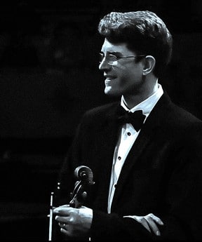 black and white photograph or a man in glasses looking over to his right holding a violin